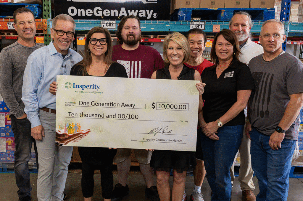 Nine people, five men and four women, smiling and holding a large check for $10,000 from Insperity to One Generation Away in a warehouse setting.