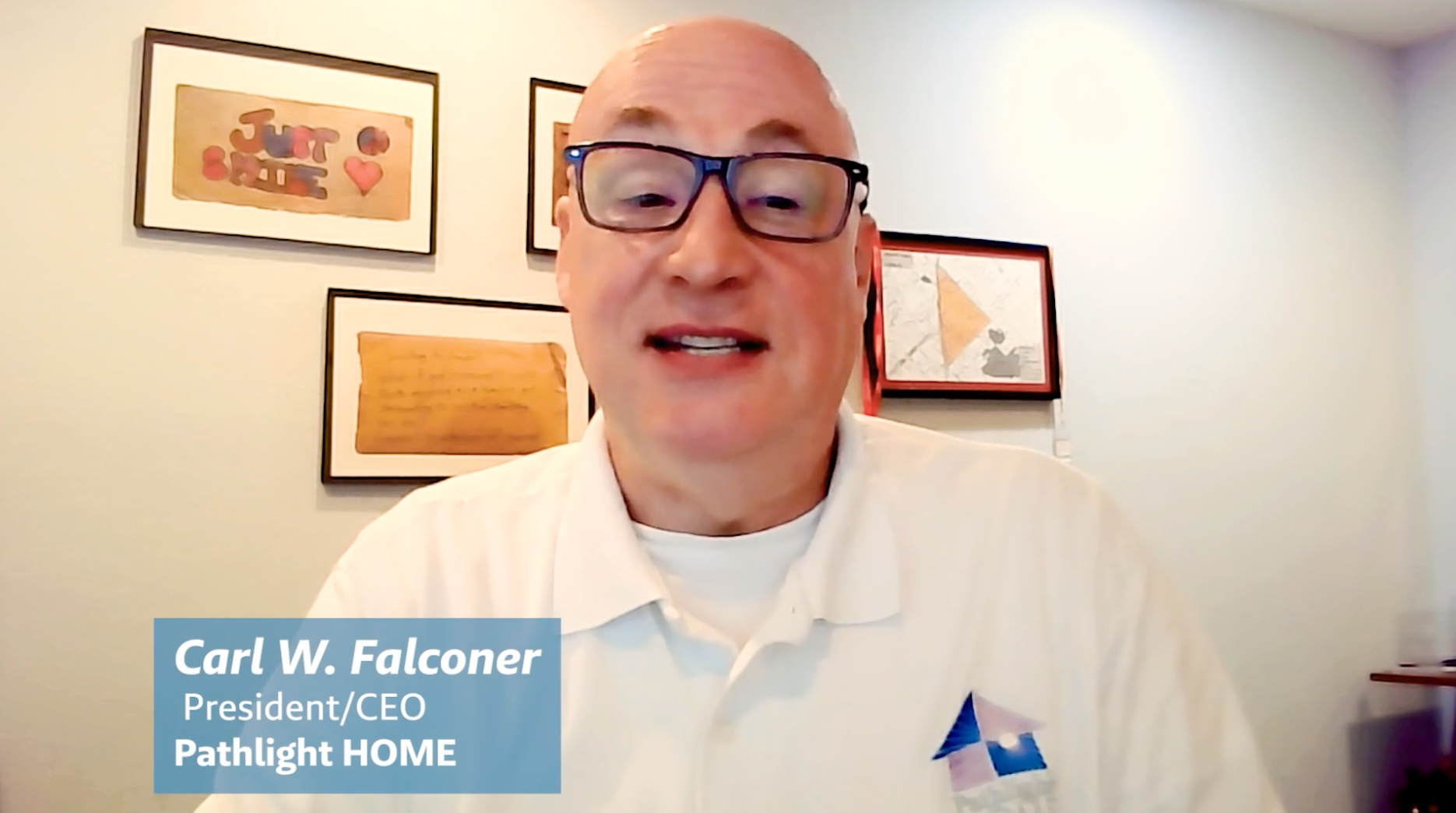 Carl W. Falconer, President/CEO of Pathlight HOME, a bald man in glasses and a white polo shirt, speaking during a video call. Three framed artworks are visible on the wall behind him.
