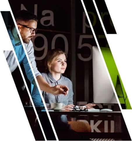A man and a woman working together, looking at a computer monitor in a dark office.
