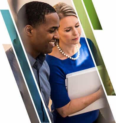 A man and a woman looking at a device, smiling and focused. The man wears a dark shirt, the woman a blue top and pearl necklace, holding a tablet.