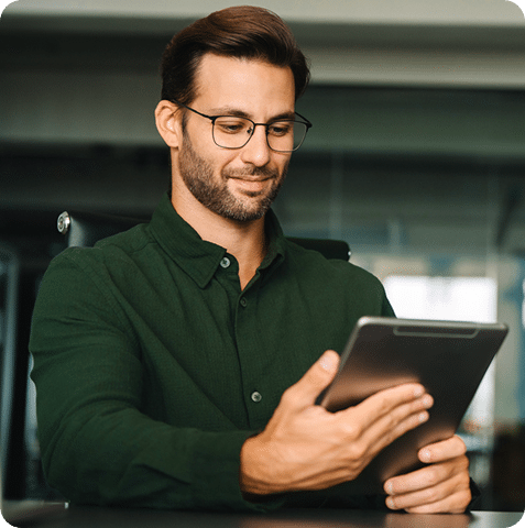 A man with glasses and a green shirt looking at a tablet.