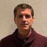 Headshot of a man with dark hair wearing a burgundy sweater.