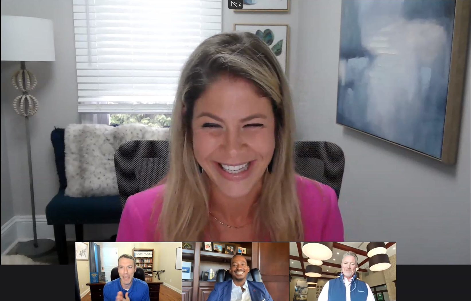 Four people participating in a video conference, with a woman in a pink top laughing joyfully in the main view, and three men smiling in smaller windows below.
