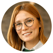 Headshot of a smiling woman with long auburn hair and cat-eye glasses.